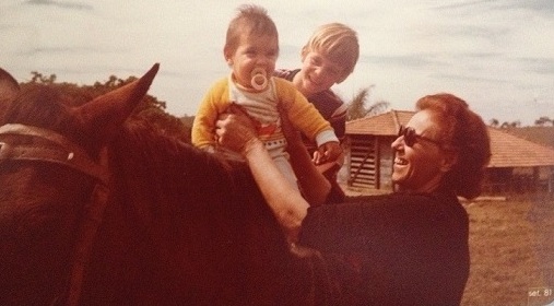 imagem de duas crianas montadas em um cavalo ajudadas pela av